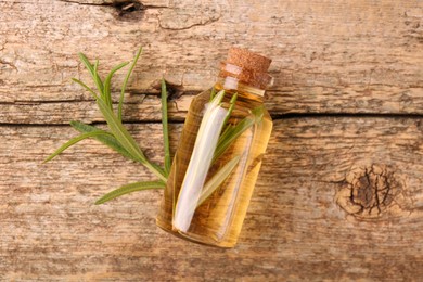 Aromatic essential oil in bottle and rosemary on wooden table, top view