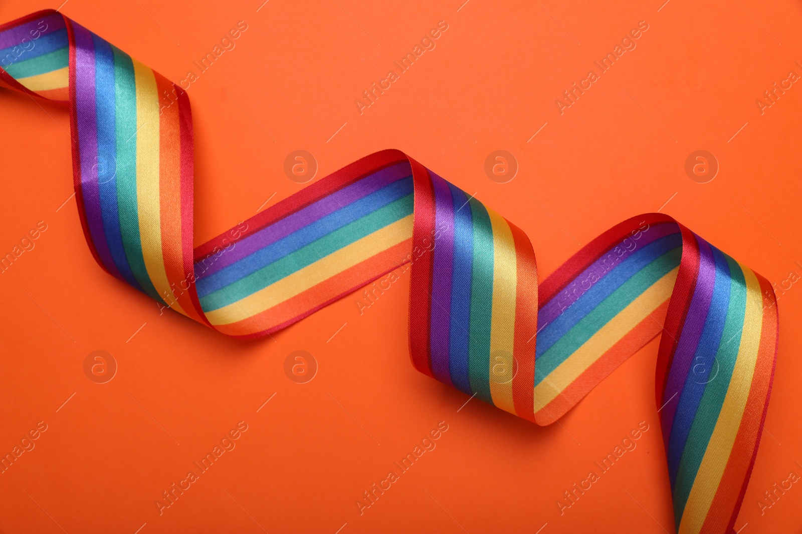 Photo of Rainbow ribbon on orange background, top view. LGBT pride