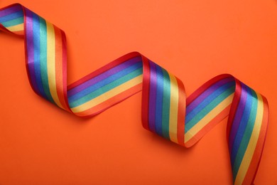 Photo of Rainbow ribbon on orange background, top view. LGBT pride
