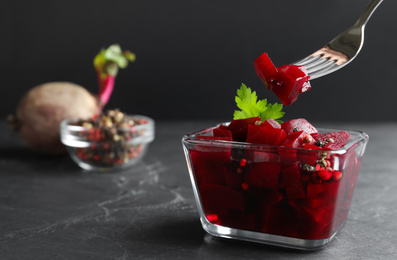 Pickled beets and fork over glass bowl on dark marble table