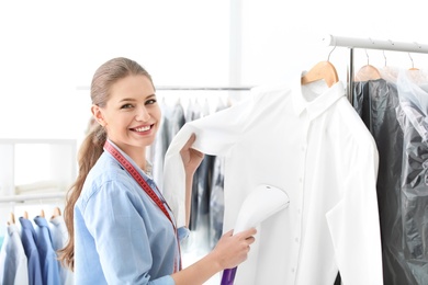 Photo of Young woman steaming shirt at dry-cleaner's