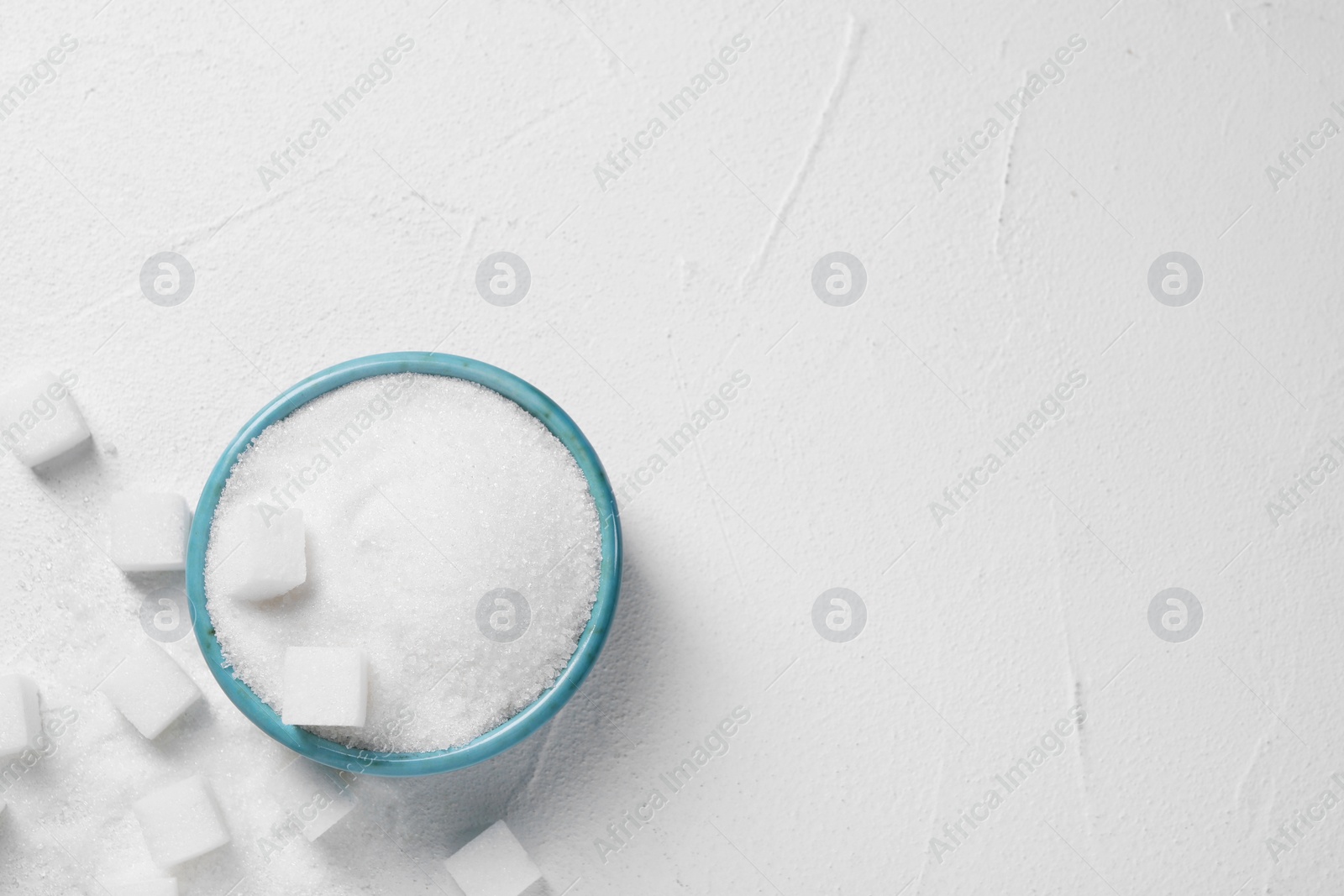 Photo of Different types of sugar in bowl on white table, flat lay. Space for text