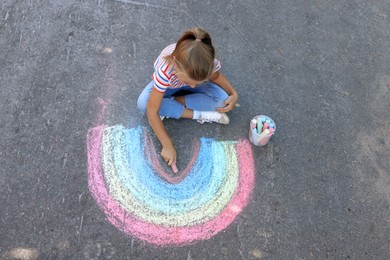 Photo of Little child drawing rainbow with colorful chalk on asphalt, above view