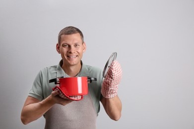 Photo of Happy man with cooking pot on light grey background. Space for text