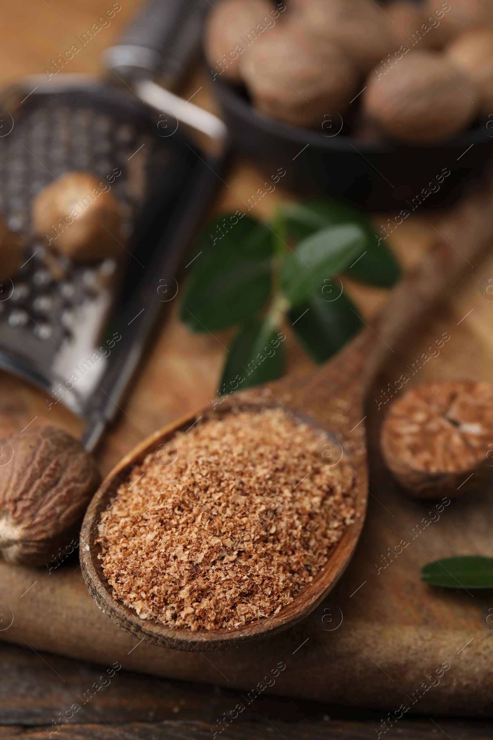 Photo of Spoon with grated nutmeg on wooden board, closeup