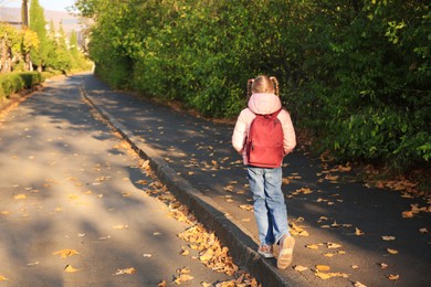 Photo of Cute little girl with backpack on city street, back view. Space for text