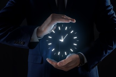 Image of Man holding virtual icon of clock on dark background, closeup. Time management