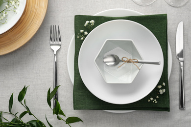 Elegant table setting with green plants on light cloth, flat lay