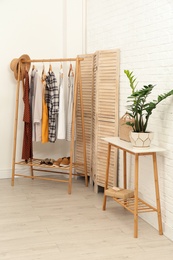 Stylish wooden table and rack with clothes in modern room interior