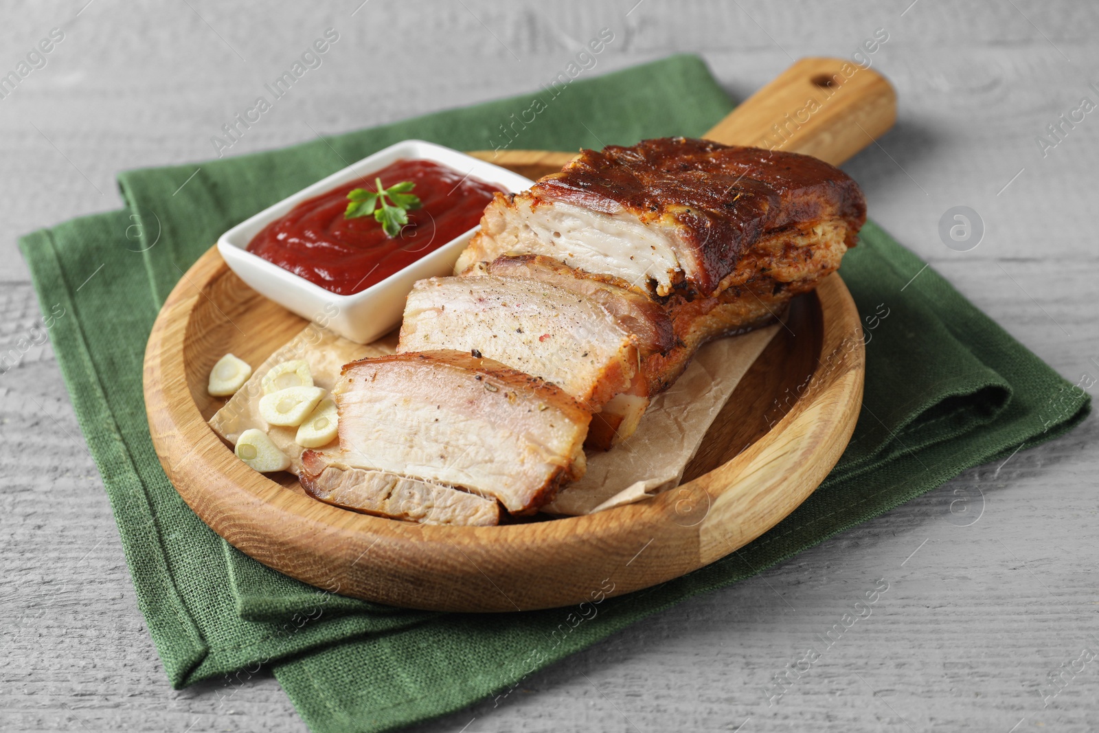 Photo of Pieces of baked pork belly served with sauce on grey wooden table