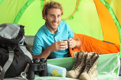 Photo of Young man in sleeping bag with mug inside of tent