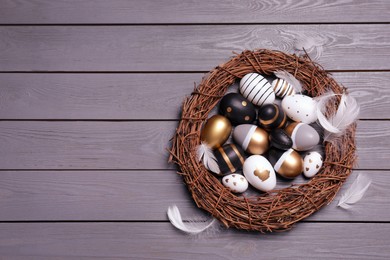 Photo of Festively decorated Easter eggs, vine wreath and feathers on grey wooden table, top view. Space for text