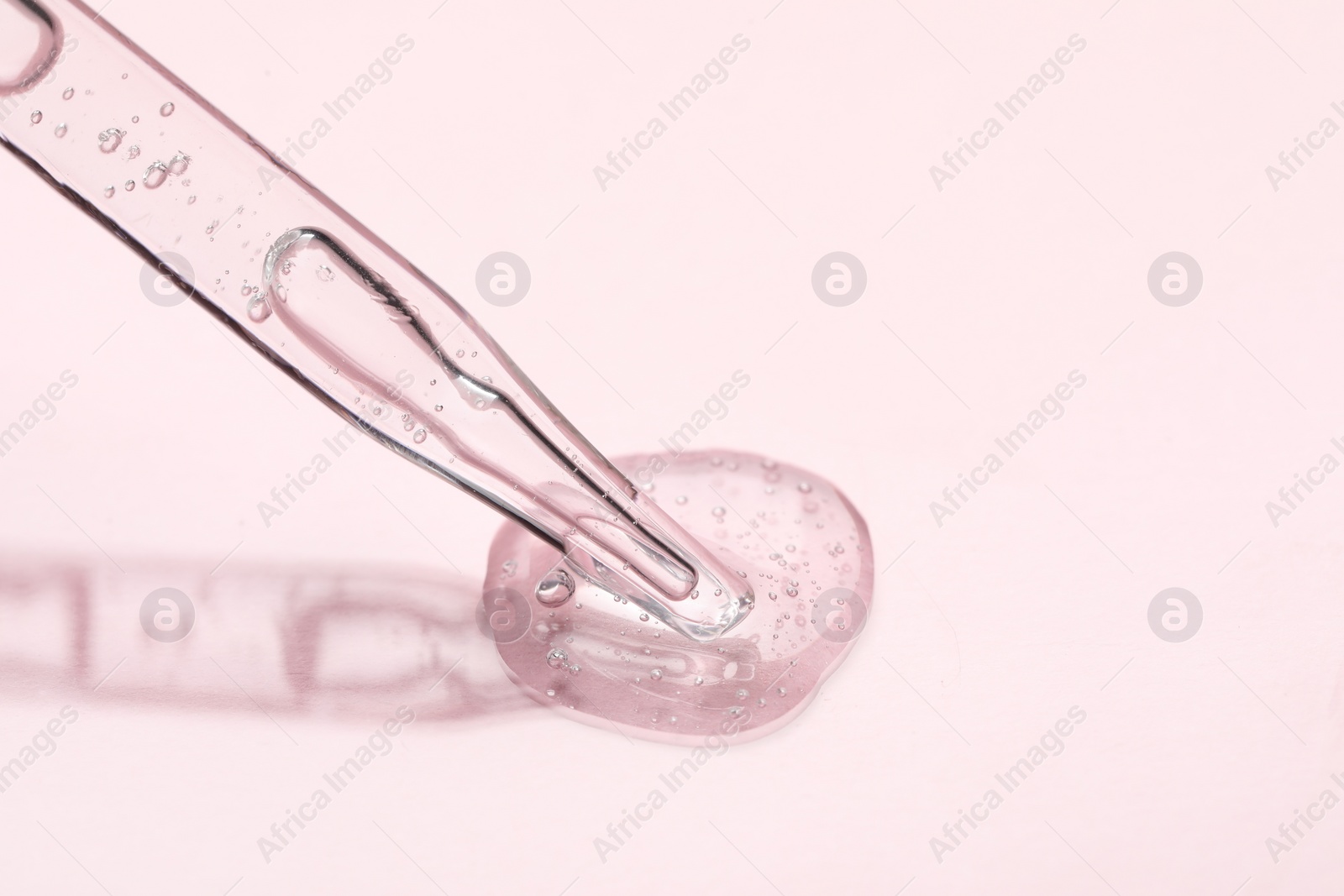 Photo of Glass pipette and transparent liquid on light pink background, closeup. Space for text