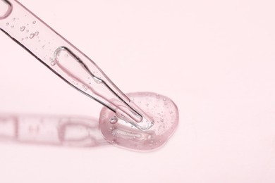 Glass pipette and transparent liquid on light pink background, closeup. Space for text