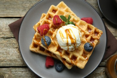 Photo of Delicious Belgian waffles with ice cream, berries and caramel sauce on wooden table, top view