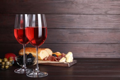 Glasses of delicious rose wine and snacks on wooden table, space for text