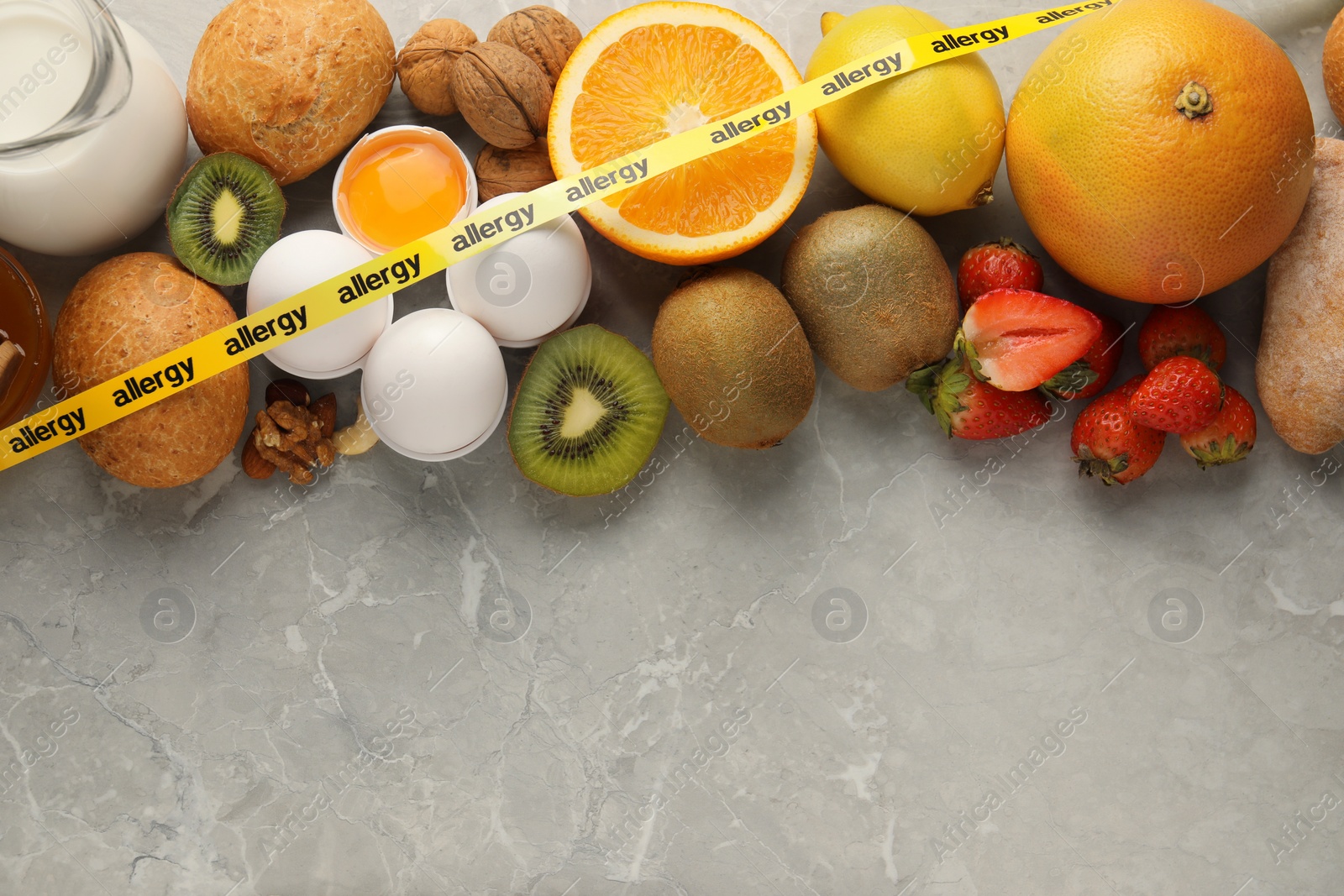 Photo of Allergenic food. Different fresh products with tape on gray marble table, top view. Space for text