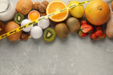 Photo of Allergenic food. Different fresh products with tape on gray marble table, top view. Space for text