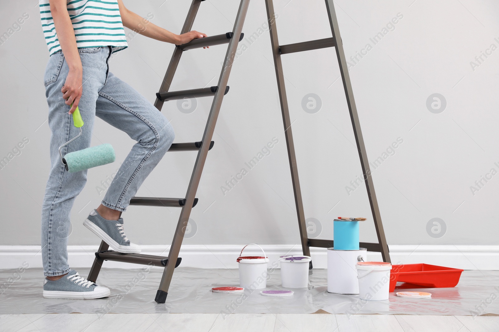 Photo of Young woman with roller near ladder indoors, closeup