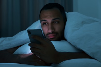 Photo of Young man using smartphone under blanket in bed at night. Internet addiction