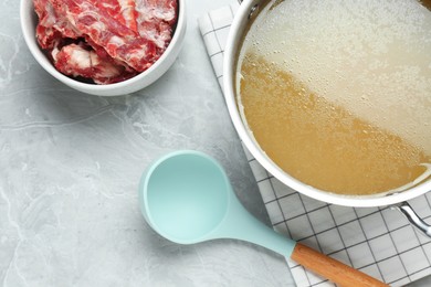 Photo of Pot with delicious broth and bowl of bones on light grey table, flat lay