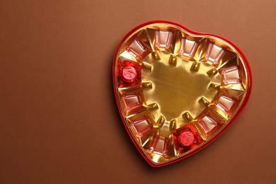 Photo of Partially empty box of chocolate candies on brown background, top view. Space for text