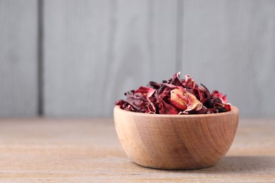 Photo of Dry hibiscus tea in bowl on wooden table, space for text