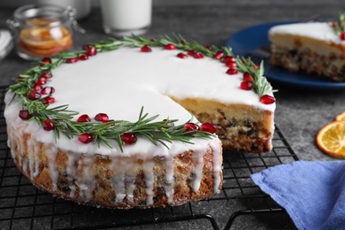 Photo of Traditional Christmas cake decorated with rosemary and pomegranate seeds on grey table, closeup