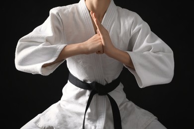 Photo of Man in keikogi with black belt on dark background, closeup. Martial arts uniform