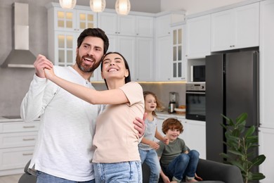 Happy family having fun at home. Couple dancing while children jumping on sofa