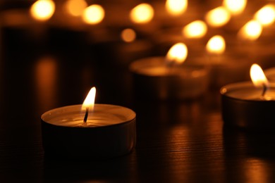 Photo of Burning candles on table in darkness, closeup. Space for text