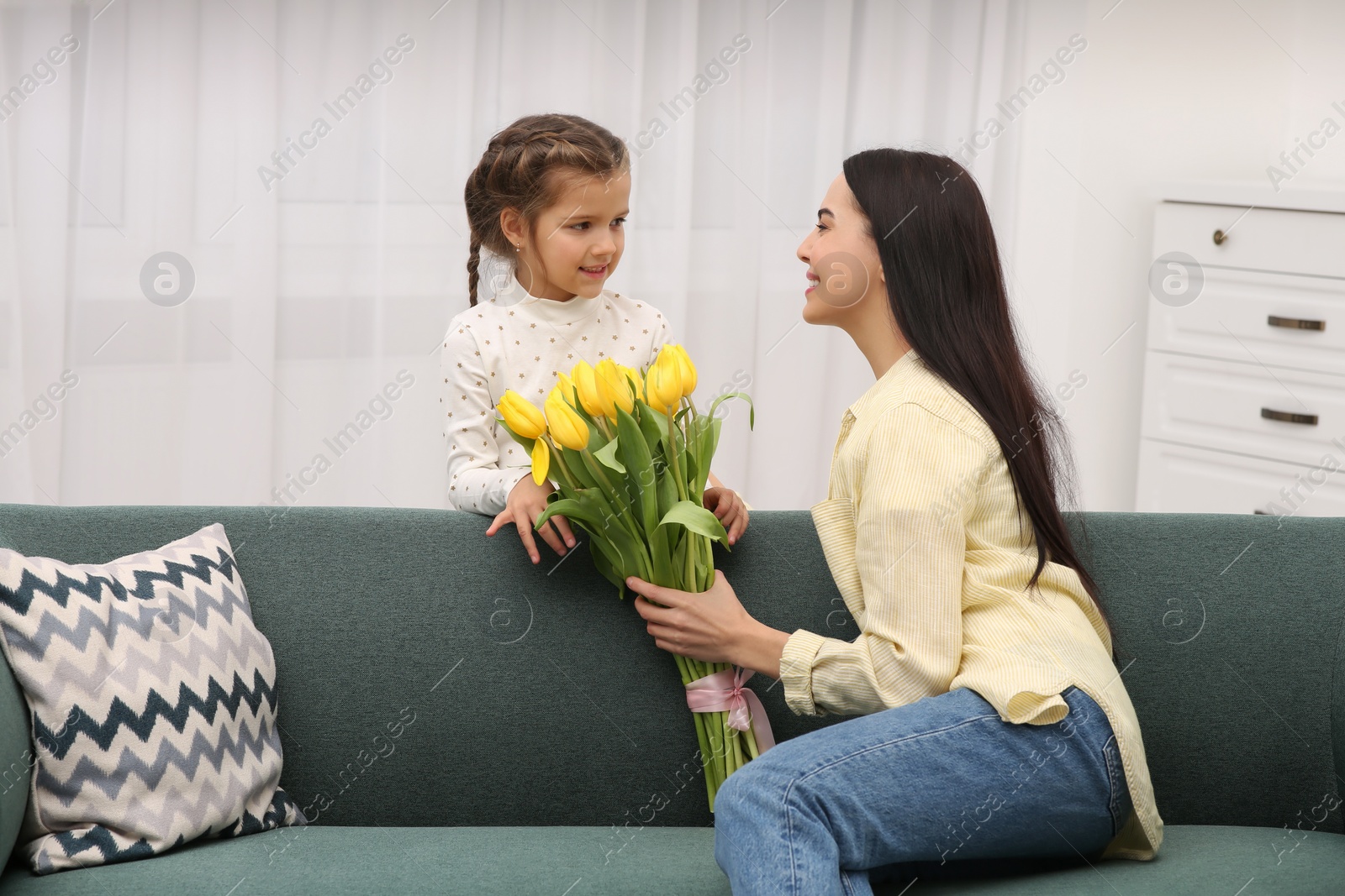 Photo of Daughter gifting happy woman bouquet of yellow tulips at home. Mother's day celebration