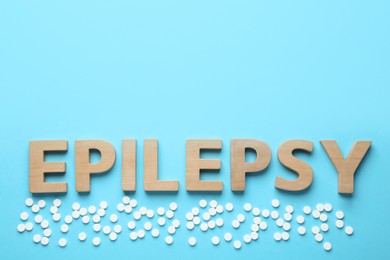Photo of Word Epilepsy and pills on light blue background, flat lay. Space for text