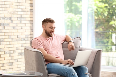 Young man using laptop while sitting in armchair at home