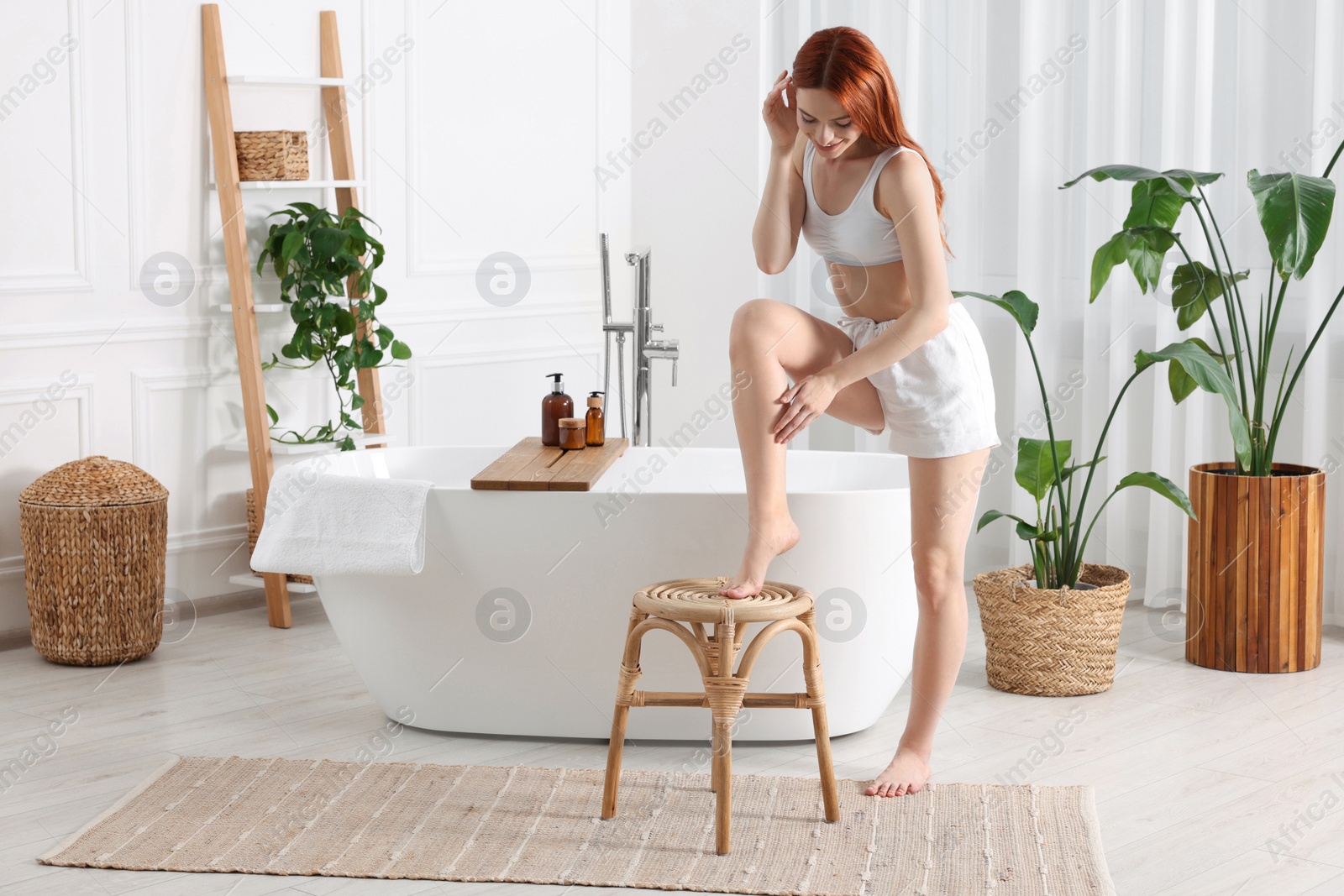 Photo of Beautiful young woman touching her smooth legs in bathroom, space for text