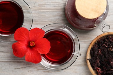 Delicious hibiscus tea and flowers on light wooden table, flat lay