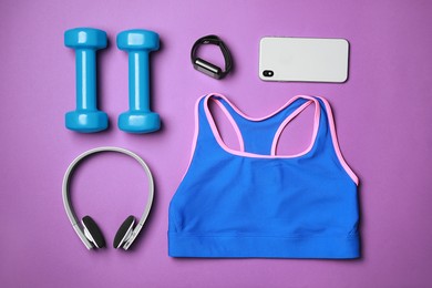 Photo of Stylish sportswear, dumbbells, smartphone and headphones on purple background, flat lay