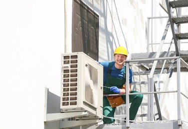 Professional technician repairing modern air conditioner outdoors