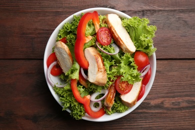 Delicious salad with chicken and vegetables on wooden table, top view