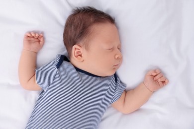 Cute newborn baby sleeping on white bed, top view