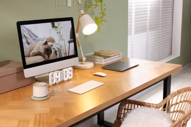 Stylish workplace with computer, laptop and lamp near olive wall at home