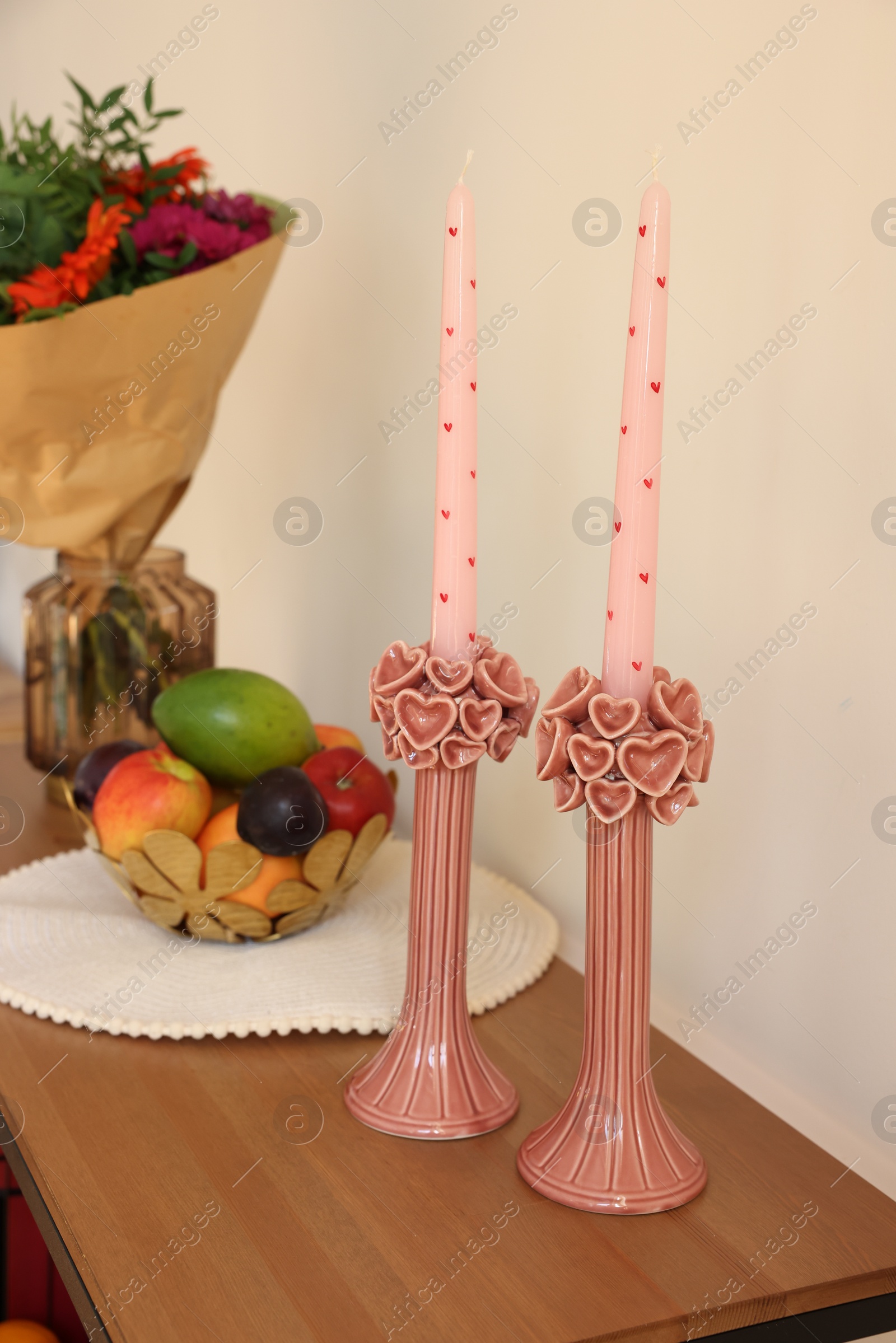 Photo of Bouquet of flowers, bowl with fresh fruits and candles on wooden table near white wall