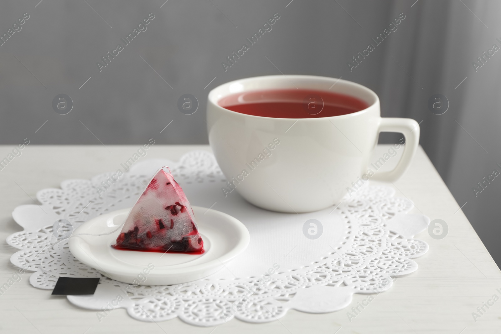 Photo of Saucer with used tea bag near cup on table