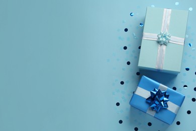 Gift boxes and shiny confetti on light blue background, flat lay. Space for text