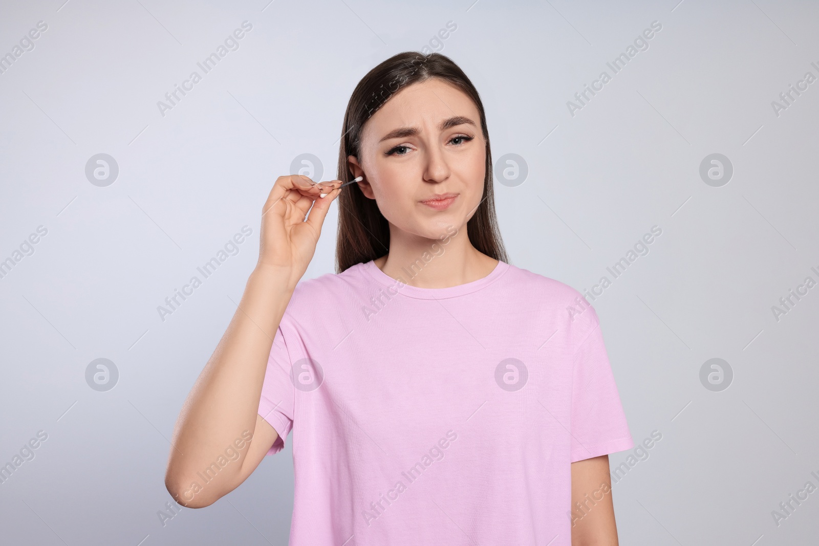 Photo of Young woman cleaning ear with cotton swab on light grey background