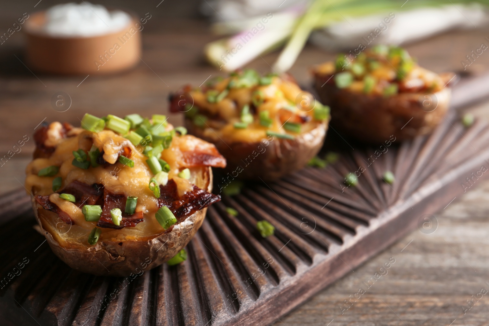 Photo of Board of baked potatoes with cheese and bacon on table, closeup