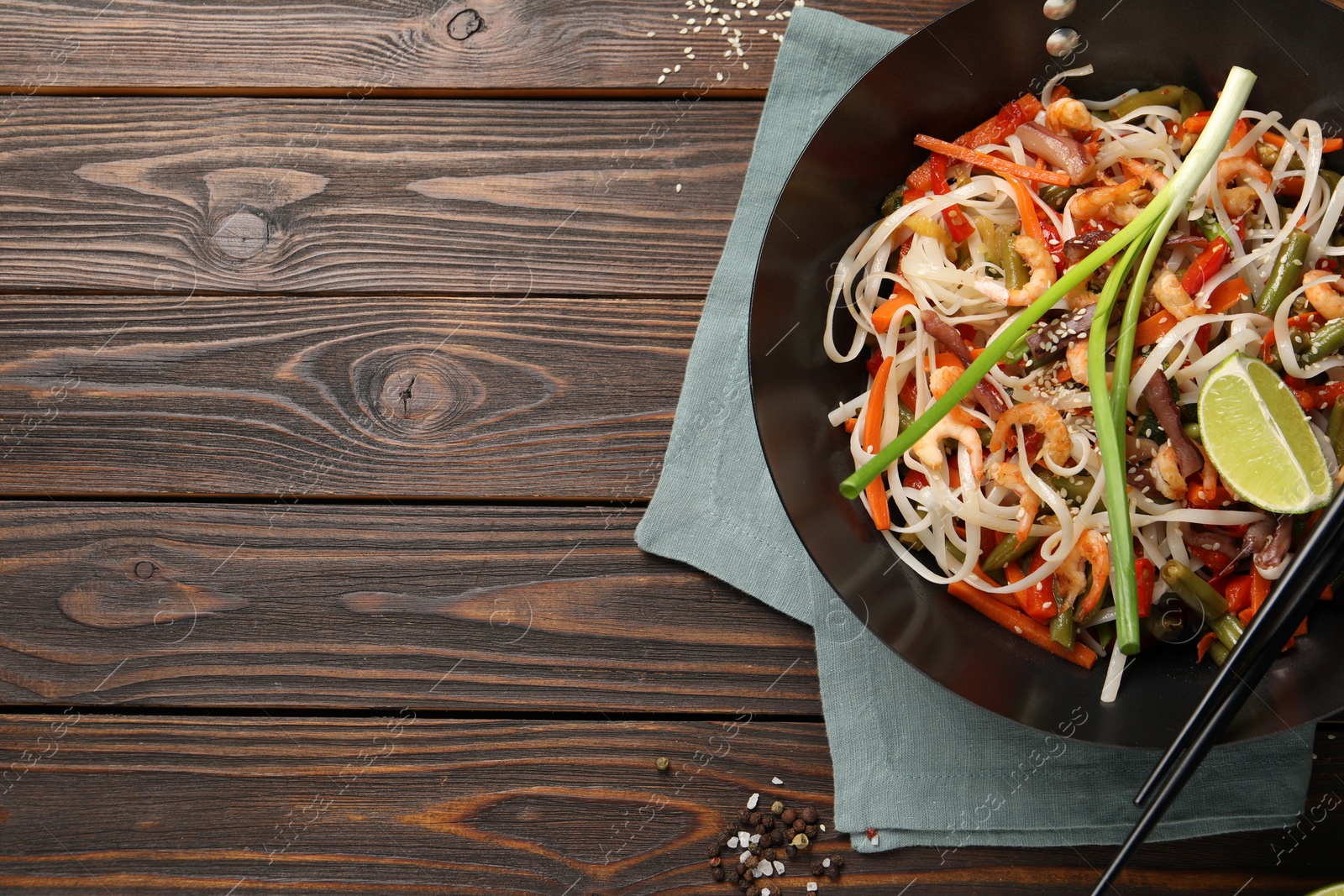 Photo of Shrimp stir fry with noodles and vegetables in wok on wooden table, top view. Space for text