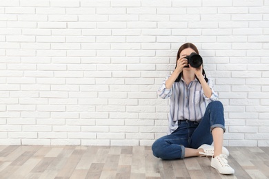 Photo of Professional photographer taking picture near white brick wall. Space for text