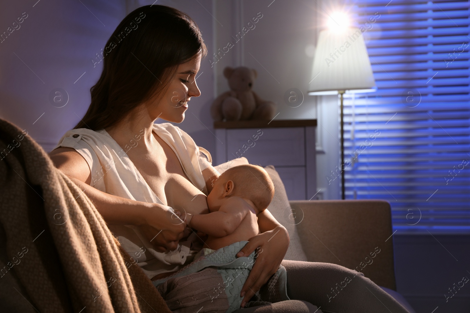 Photo of Young woman breastfeeding her little baby indoors at night