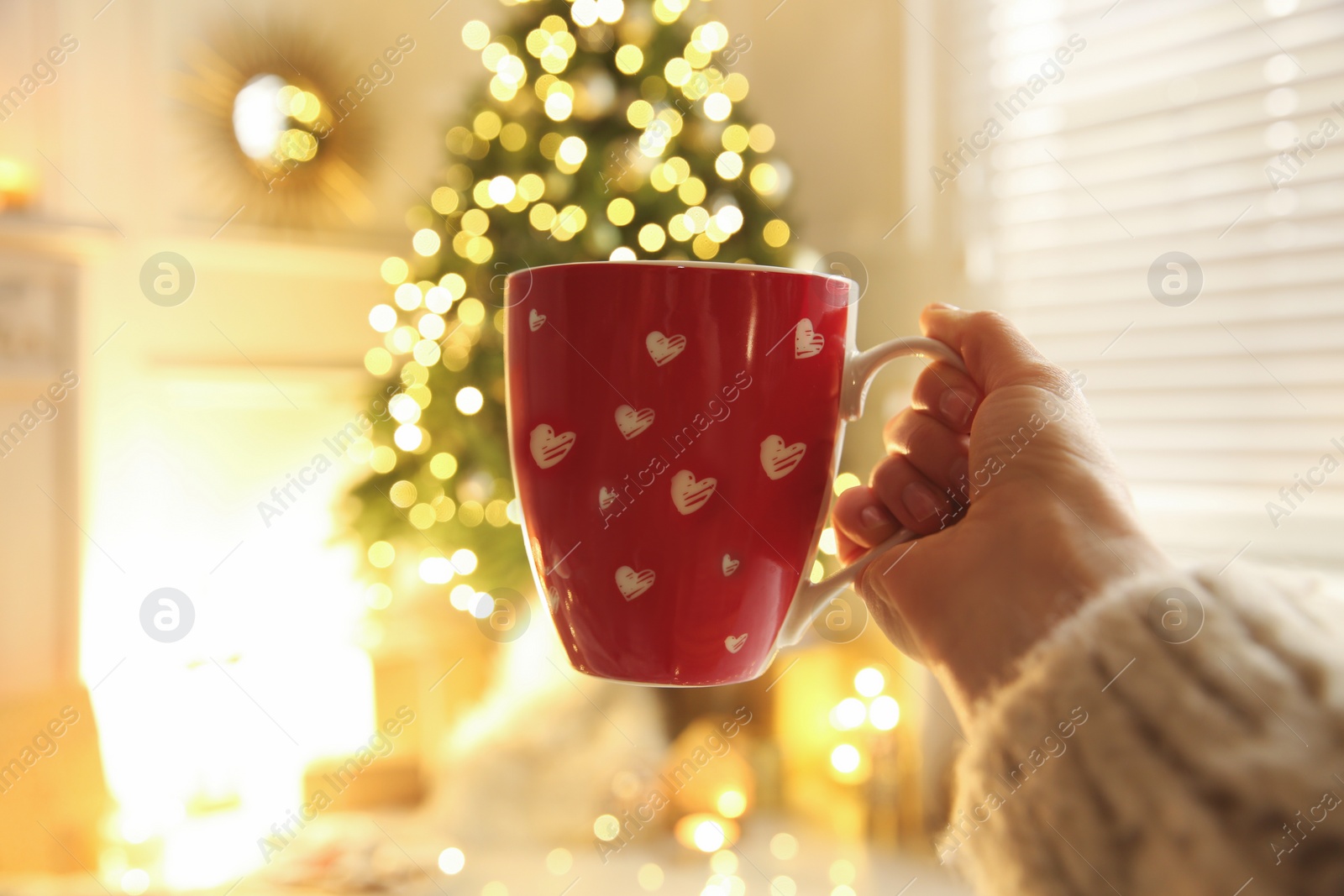 Photo of Woman with cup of drink and blurred Christmas tree on background, closeup